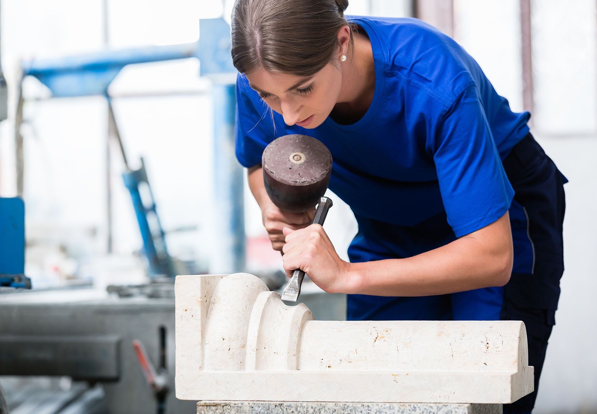 Junge Frau arbeitet mit Hammer und Meißel an einem Steinblock in der Werkstatt